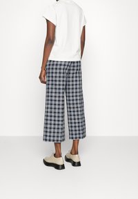 Vit kortärmad topp i kombination med marinblå och vit rutiga vida byxor. Beige skor med svart sula fulländar looken.