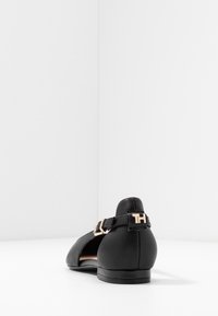 Schwarze Flatschuhe mit runder Zehenpartie, aus glattem Leder, mit einem Knöchelriemen und einer goldfarbenen Schnalle sowie einem niedrigen Absatz.