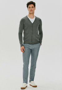 Szary kardigan zapinany na guziki na białej koszuli, w połączeniu z jasnoniebieskimi spodniami i białymi trampkami. Gładka tekstura, dopasowany krój.