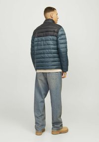 Giacca a vento con la parte inferiore blu e la parte superiore nera. Presenta cuciture orizzontali, materiale leggero e colletto.