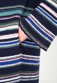 Szydełkowy sweter w poziome paski w kolorze granatowym, zielonym, różowym i białym. Teksturowana tkanina, z kieszenią i kontrastowym wykończeniem na mankietach.