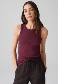 Burgunderfarbener gerippter Tank-Top mit rundem Ausschnitt, kombiniert mit lockeren schwarzen Leinenhosen. Das Tank-Top hat eine figurbetonte Passform und ärmelloses Design.