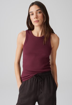 Burgundy ribbed tank top with a round neckline, paired with loose black linen pants. The tank features a fitted cut and sleeveless design.