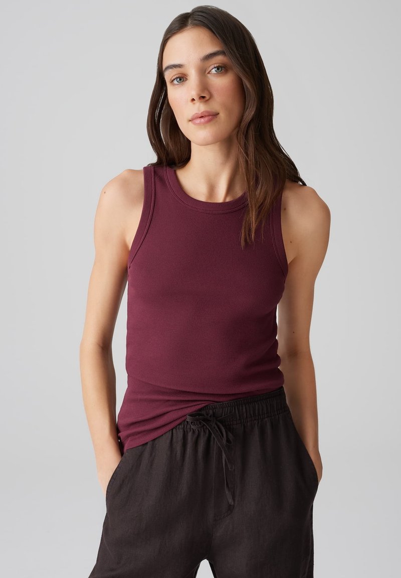 Burgunderfarbener gerippter Tank-Top mit rundem Ausschnitt, kombiniert mit lockeren schwarzen Leinenhosen. Das Tank-Top hat eine figurbetonte Passform und ärmelloses Design.