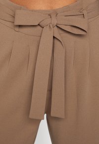 Brązowe spodnie z wysokim stanem z materiałowym paskiem z kokardą, zaprasowanym wzorem i gładką teksturą.