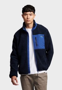 Fleecejacke in Marineblau mit einem blauen Einsatz, durchgehendem Reißverschluss, Reißverschlusstasche auf der Brust und strukturiertem Stoff. Mit Stehkragen und lockerer Passform.