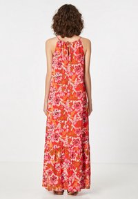 Robe maxi en tissu rouge ornée de motifs floraux vibrants en rose et blanc, avec un col halter et un bas fluide à volants.