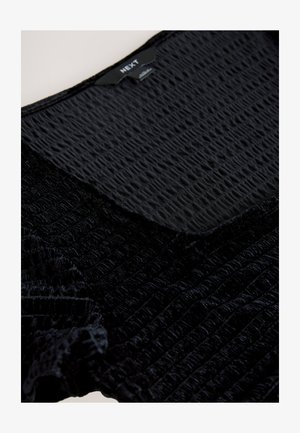 Sort tekstureret top med krøllet stof og en glat sektion ved halsudskæringen, med synligt mærke i midten.