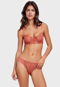 Reggiseno in pizzo e slip coordinato in corallo, con motivi floreali, texture morbide, spalline sottili e dettagli in pizzo sagomato.