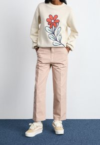 Pull crème avec motif de fleur rouge ; pantalon rose clair ; baskets crème et beige ; coupe décontractée. Tricot texturé et textures de tissu lisse.