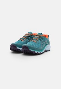 Chaussures de trail en teal avec un dessus en mesh texturé, accents orange vif, logo réfléchissant et semelle violette robuste pour une meilleure traction.