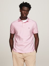 Roze katoenen polo met een kraag, doorlopende knoopsluiting en geborduurd logo; gecombineerd met lichtbeige shorts.