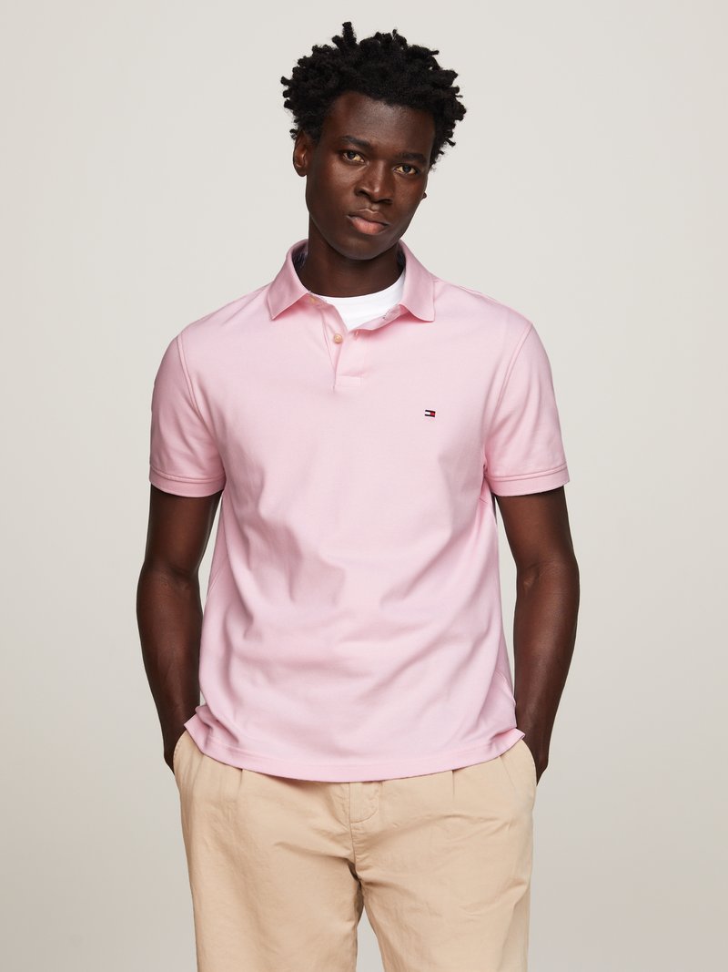 Roze katoenen polo met een kraag, doorlopende knoopsluiting en geborduurd logo; gecombineerd met lichtbeige shorts.