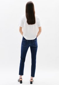 Donkerblauwe jeans met een slim fit, voorzien van achterzakken en een licht verkorte lengte, gecombineerd met een witte top met korte mouwen.
