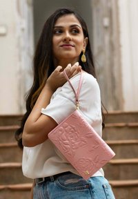 Roze reliëf portemonnee met bloemen- en vlinderpatronen, voorzien van een polsband en gouden hardware accenten. Gladde leertextuur.