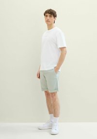 Biała bawełniana koszulka z okrągłym dekoltem, zestawiona z jasnobeżowymi, podwiniętymi szortami oraz białymi trampkami z teksturowaną podeszwą.