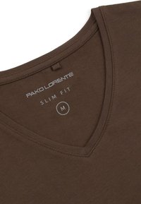 Brązowa koszulka slim-fit z dekoltem w serek. Wykonana z miękkiego materiału, posiada metkę z nazwą marki, rozmiarem i szczegółami dopasowania.
