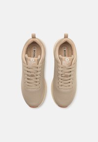 Zapatillas de malla beiges con punta redonda, cordones planos y suela de goma. Presentan un collar y una plantilla acolchados, con un logotipo en la lengüeta.