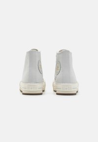 Zapatillas altas de lona gris claro con un parche de logo redondo, suela de goma blanca y acentos beige. Detalles de costura en las costuras.