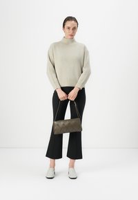 Maglione beige a costine con colletto alto, pantaloni neri a campana e scarpe slip-on grigio chiaro; tiene una borsa a tracolla marrone scuro, trapuntata.