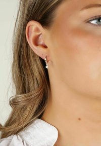 Silverhängörhängesmycke med en hängande stjärnformad charm, som har en klar ädelsten. Slät yta, blank yta och en liten spänne.