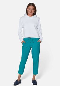Witte hoodie met een ontspannen pasvorm, gecombineerd met teal kleurige joggers en marineblauwe loafers. Zacht materiaal, casual design, enkel lengte broek.