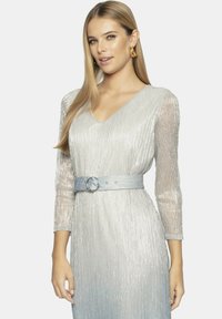 Srebrna sukienka z pionową żebrowaną teksturą, dekoltem w kształcie litery V i rękawami o długości trzech czwarte. Posiada niebieski pasek z okrągłą klamrą.