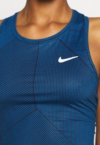 Gros plan d'une personne portant un haut de sport sans manches Nike rayé bleu et noir avec un logo swoosh blanc sur la poitrine.
