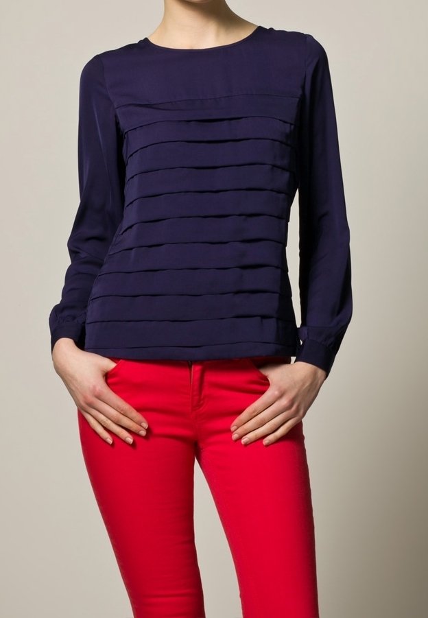 Blusa azul marino de manga larga con pliegues horizontales; escote redondo y silueta ajustada. Combinada con vaqueros pitillo rojos. Textura de tela suave.