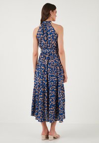 Robe maxi bleue à col halter avec un motif floral marron, taille froncée, jupe à volants et tissu doux, vue de dos.