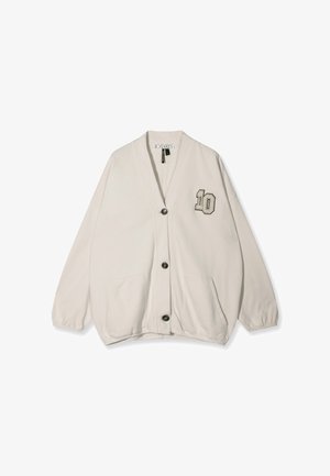 Jasno beżowy kardigan wykonany z miękkiego materiału, z dekoltem w kształcie V, czarnymi guzikami, dwoma przednimi kieszeniami i haftowanym „10” po lewej stronie.