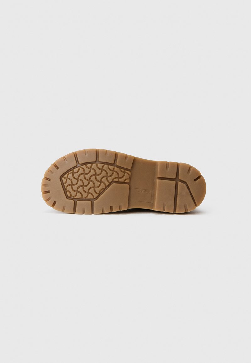 Brown rubber shoe sole with a wave pattern, textured grip, and prominent lugs. Reinforced heel and distinct design features throughout.