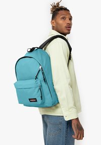 Mochila turquesa con un compartimento principal y un bolsillo frontal con cremallera, con acentos en negro y correas ajustables para los hombros.