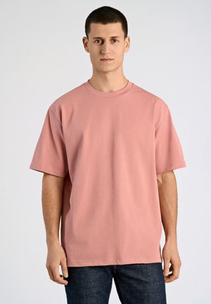 Camiseta de algodón rosa con cuello redondo y mangas cortas, con un corte relajado y textura suave. Llevada con jeans de mezclilla oscura.