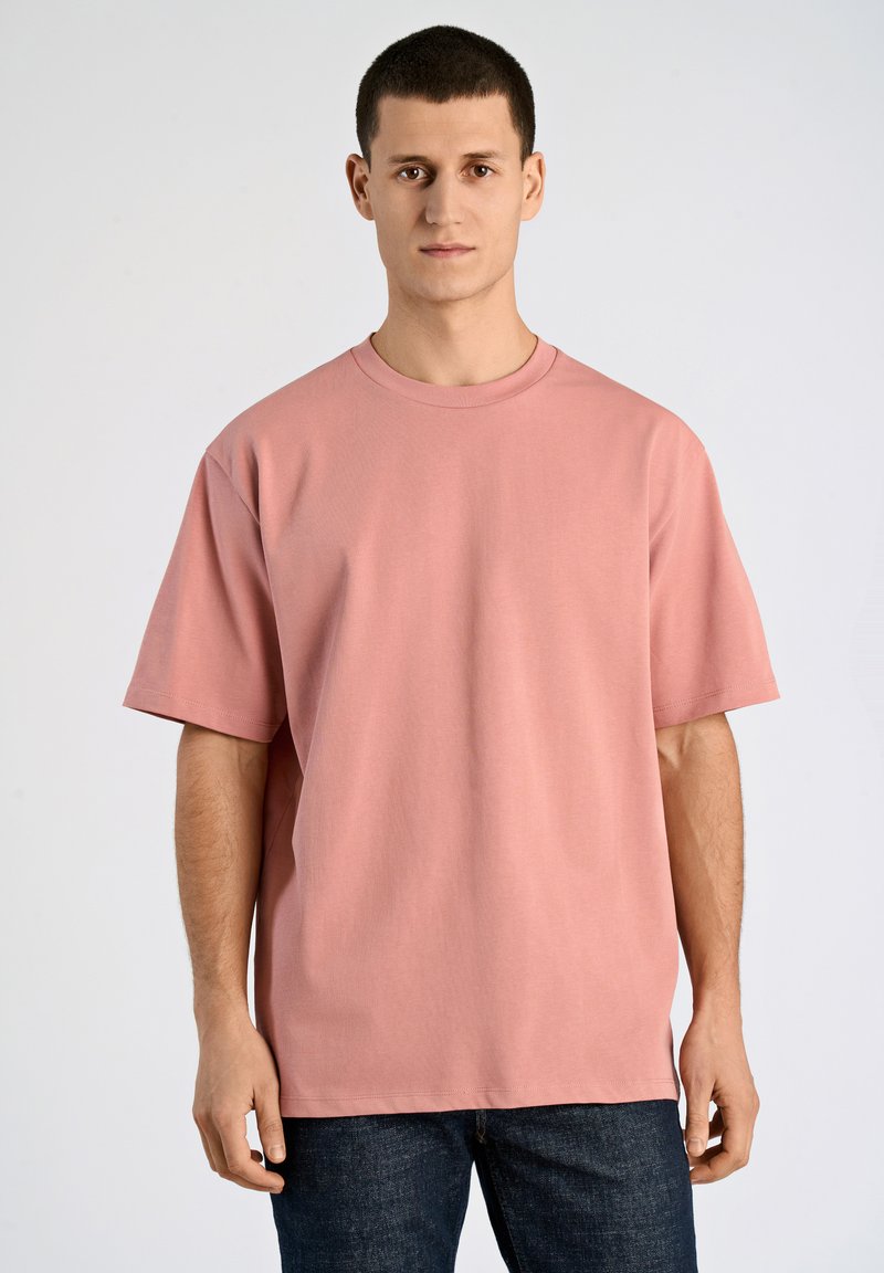 Rosa bomullströja med rundad halsringning och korta ärmar, med en avslappnad passform och mjuk textur. Bärs tillsammans med mörka denimjeans.