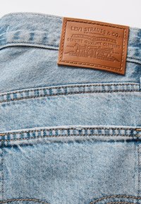 Világoskék farmeranyag bőr folttal, amelyen a "Levi Strauss & Co." felirat domborított részletekkel. Jellegzetes varrás a zsebek mentén.