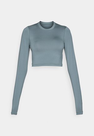 Long-sleeved, cropped top in soft, stretchy light blue fabric with a round neckline and subtle logo detail at the center front.