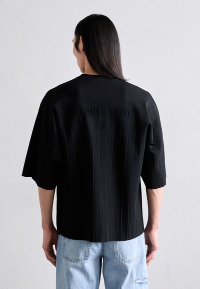 Czarna, oversize koszula z wertykalnymi teksturowanymi paskami. Na plecach znajduje się wytłoczone "HELMUT LANG". W połączeniu z jasnoniebieskimi dżinsami.