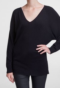Pull noir en V en tricot doux, avec une coupe décontractée, des épaules dropées et un ourlet et des poignets côtelés. Texture lisse.
