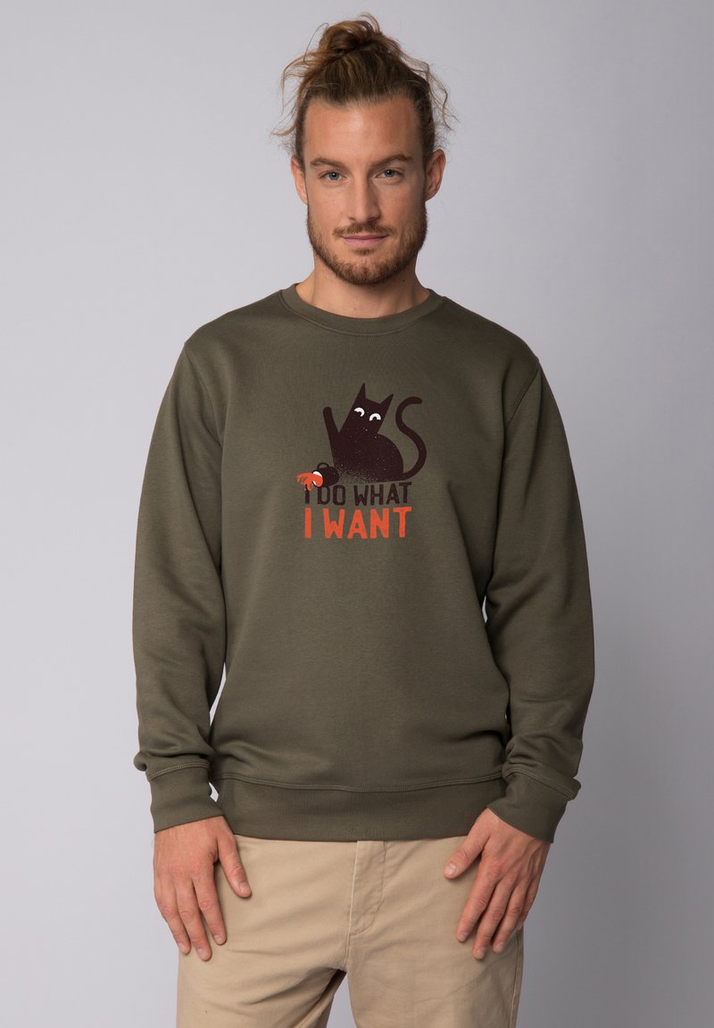 Olijfgroene sweatshirt van katoen met een speelse afbeelding van een zwarte kat en de tekst "IK DOE WAT IK WIL" in gedurfde, contrasterende kleuren.