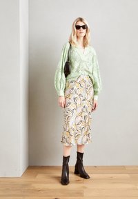 Svetlozelená blúzka s textúrovaným dizajnom, vzorovaná sukňa strednej dĺžky v pastelových farbách a čierne čižmy na podpätku. Celý outfit dopĺňa jednoduchá kabelka.
