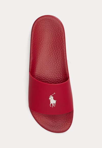 Czerwona sandałka na płaskim obcasie z teksturowaną wkładką i białym logo gracza polo na szerokim pasku na górze stopy.