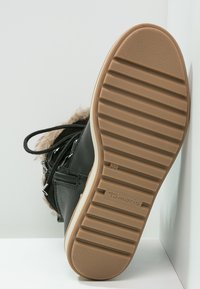 Bota de cuero sintético negra con una suela de goma texturizada en tono marrón, con detalles de cremallera y un forro suave de piel alrededor del tobillo. Talla 36.