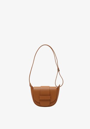 Brązowa skórzana torba na ramię o zakrzywionym kształcie, z fakturowanym wykończeniem i przednią klapką. Modelka ma na sobie zielony sweter i niebieskie dżinsy.