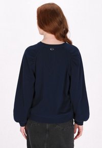 Felpa blu scuro a girocollo con maniche a sbuffo e polsini elastici; presenta un piccolo logo sulla parte posteriore del collo.