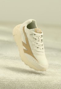Adidași albi cu accente bej, partea superioară din plasă, talpă texturată și design cu șireturi. Prezintă branding-ul "HI-TEC" și "SHADOW".