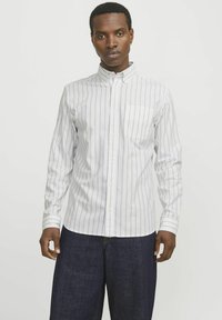 Witte longsleeve shirt met verticale blauwe strepen, button-down kraag, enkel borstzakje en gestructureerde stof, gecombineerd met donkere denim broek.
