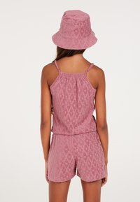 Conjunto de toalla de color rosa con una parte superior ajustada y pantalones cortos, que presenta un patrón texturizado; combinado con un sombrero de cubo a juego.