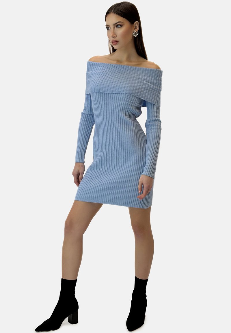 Abito off-the-shoulder a righe blu chiaro con maniche lunghe, forma aderente e lunghezza fino a metà coscia, abbinato a stivaletti a calza neri.