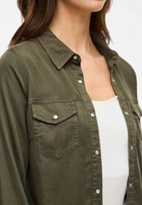 Camicia verde oliva con bottoni, in tessuto leggero, colletto, due tasche sul petto con bottoni a pressione, cuciture visibili, vestibilità comoda.